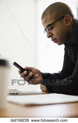 Stock Photo - Mixed race businessman using cell phone at desk. Fotosearch