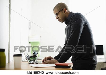 Stock Image - Mixed race businessman working on laptop at desk. Fotosearch