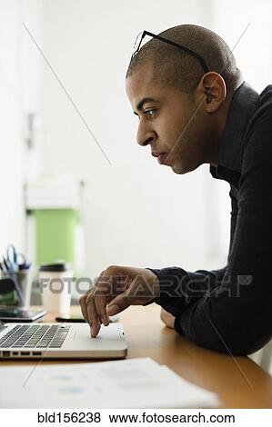 Stock Photo - Mixed race businessman working on laptop at desk. Fotosearch