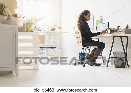 Stock Image - Mixed race businesswoman using cell phone at desk. Fotosearch