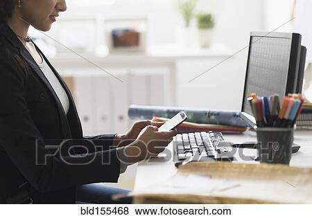 Mixed race businesswoman using cell phone at desk View Large Photo Image Stock Photo - Mixed race businesswoman using cell phone at desk. Fotosearch