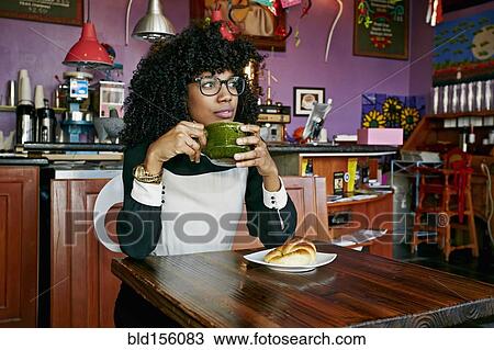 Stock Image - Mixed race woman drinking coffee in cafe. Fotosearch