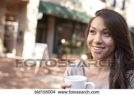 Picture - Mixed race woman drinking coffee on sidewalk. Fotosearch