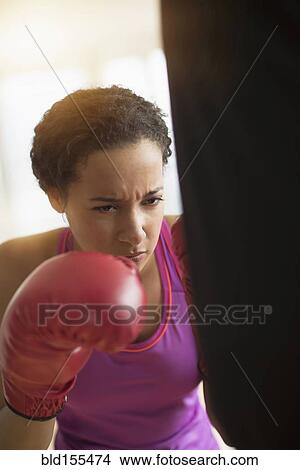 Picture - Mixed race woman hitting punching bag in gym. Fotosearch