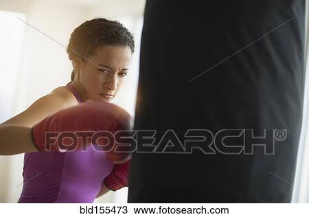 Stock Image - Mixed race woman hitting punching bag in gym. Fotosearch