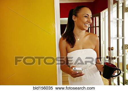 Stock Photography - Mixed race woman holding cell phone and coffee cup in doorway. Fotosearch