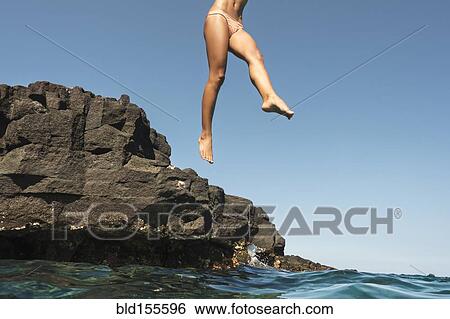 Stock Photograph - Mixed race woman jumping from rocks into ocean. Fotosearch