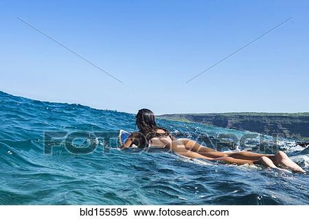 Stock Photography - Mixed race woman laying on surfboard in ocean waves. Fotosearch