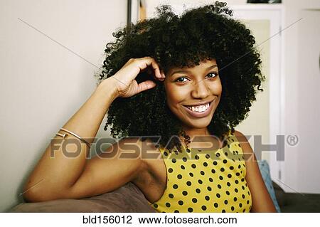 Stock Image - Mixed race woman smiling on sofa. Fotosearch