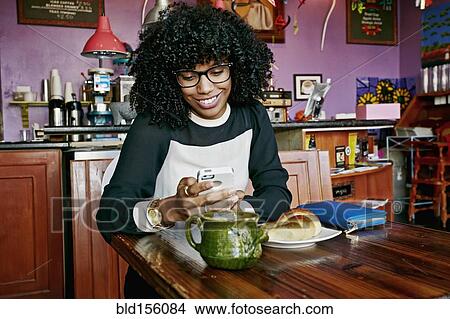 Picture - Mixed race woman using cell phone in cafe. Fotosearch