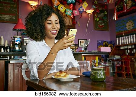 Stock Image - Mixed race woman using cell phone in cafe. Fotosearch