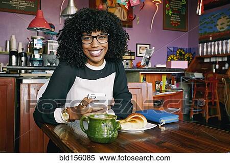 Stock Photography - Mixed race woman using cell phone in cafe. Fotosearch