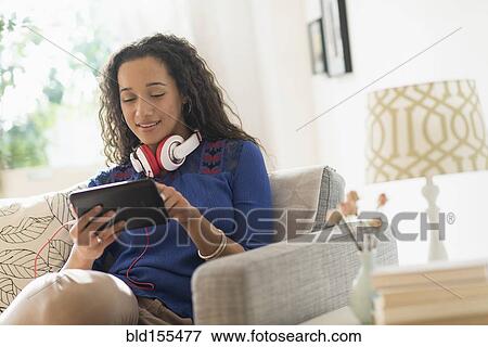 Stock Photo - Mixed race woman using digital tablet on sofa. Fotosearch