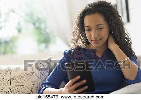 Stock Photo - Mixed race woman using digital tablet on sofa. Fotosearch