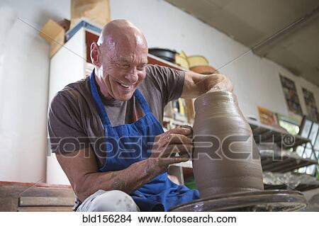 Picture - Older Caucasian man forming pottery on wheel in ceramics studio. Fotosearch