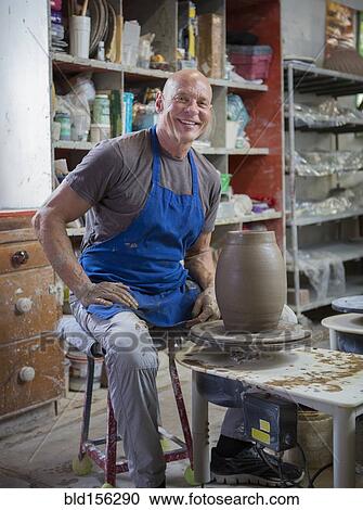 Stock Image - Older Caucasian man forming pottery on wheel in ceramics studio. Fotosearch