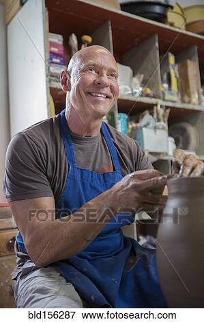 Stock Photo - Older Caucasian man forming pottery on wheel in ceramics studio. Fotosearch