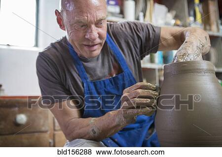 Stock Photo - Older Caucasian man forming pottery on wheel in ceramics studio. Fotosearch