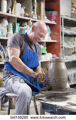 Stock Photography - Older Caucasian man forming pottery on wheel in ceramics studio. Fotosearch