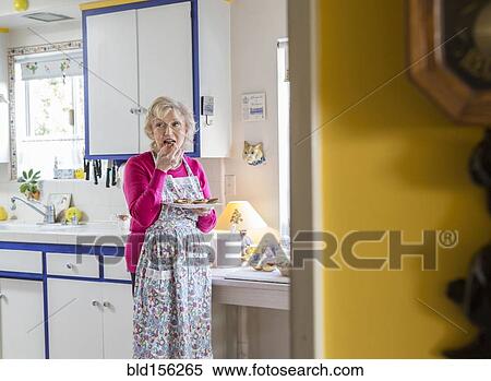 Stock Photography - Older Caucasian woman eating in kitchen. Fotosearch
