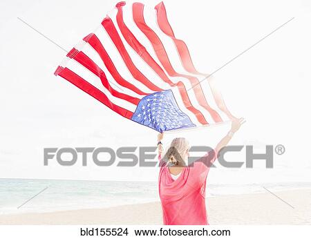 Picture - Older Caucasian woman holding American flag on beach. Fotosearch