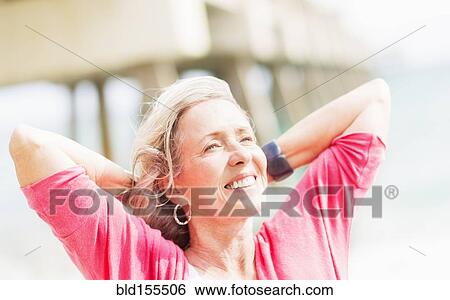 Stock Photograph - Older Caucasian woman with hands behind head on beach. Fotosearch