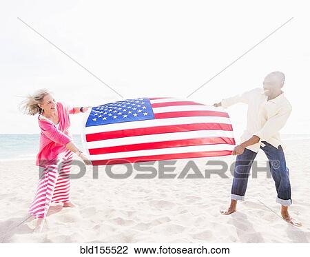 Stock Image - Older couple holding American flag on beach. Fotosearch