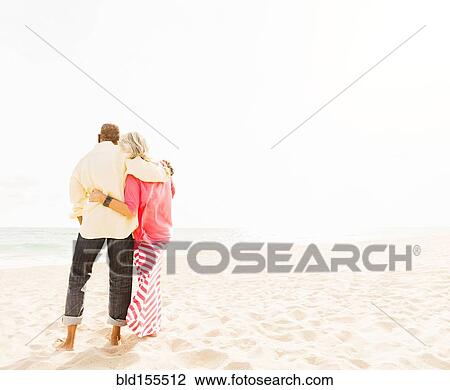 Stock Image - Older couple hugging on beach. Fotosearch