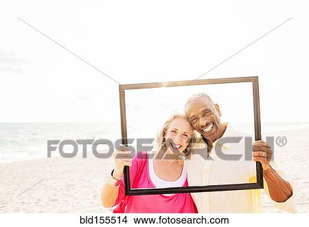 Picture - Older couple posing in picture frame on beach. Fotosearch