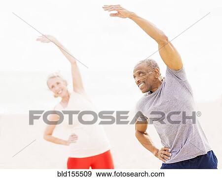 Stock Photo - Older couple stretching together on beach. Fotosearch
