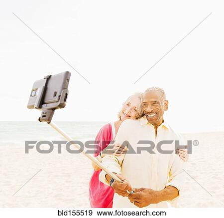Stock Photo - Older couple taking cell phone photograph on beach. Fotosearch