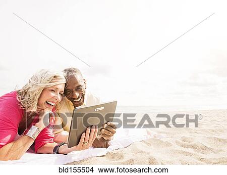 Picture - Older couple using digital tablet on beach. Fotosearch