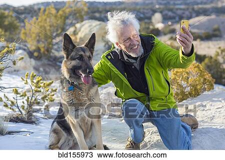 Stock Image - Older man taking cell phone photograph with dog on rock formations. Fotosearch