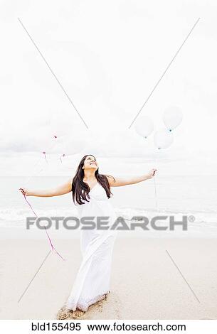 Stock Photography - Pregnant mixed race woman holding balloons on beach. Fotosearch