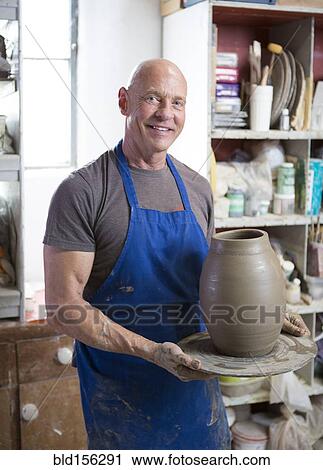 Stock Image - Proud older Caucasian man holding pottery in ceramics studio. Fotosearch
