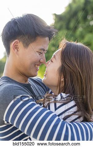 Stock Image - Smiling Korean couple hugging in park. Fotosearch