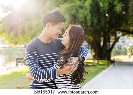 Stock Photo - Smiling Korean couple hugging in park. Fotosearch