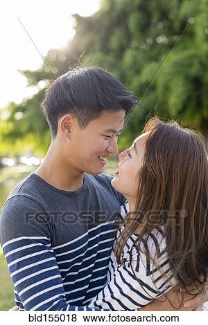 Stock Photo - Smiling Korean couple hugging in park. Fotosearch