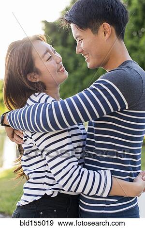 Stock Photo - Smiling Korean couple hugging in park. Fotosearch