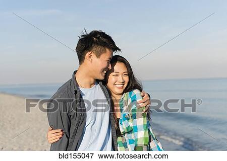 Stock Photo - Smiling Korean couple hugging on beach. Fotosearch
