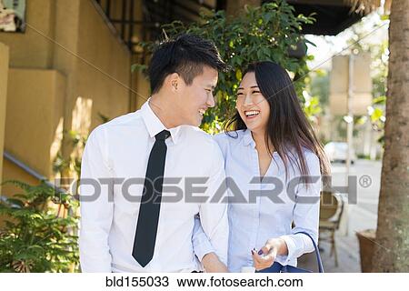 Stock Image - Smiling Korean couple walking on sidewalk. Fotosearch