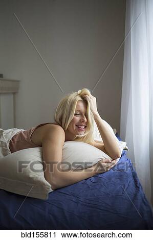 Stock Image - Smiling woman laying in bed. Fotosearch