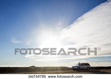 Stock Photography - Sunshine and clouds over car on roadside. Fotosearch