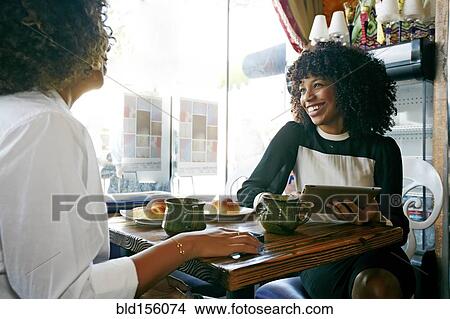 Picture - Women using digital tablet and drinking coffee in cafe. Fotosearch
