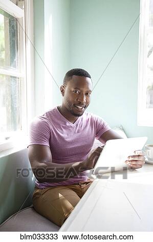 Stock Image - Black man using digital tablet at table. Fotosearch