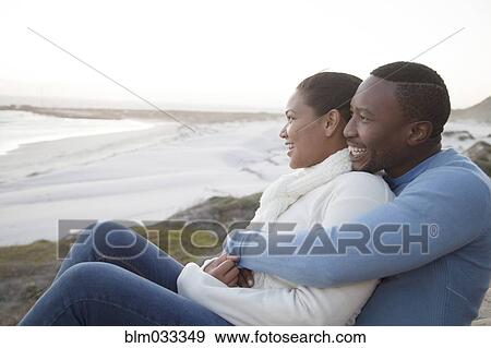 Stock Photo - Couple hugging on cliffs over beach. Fotosearch