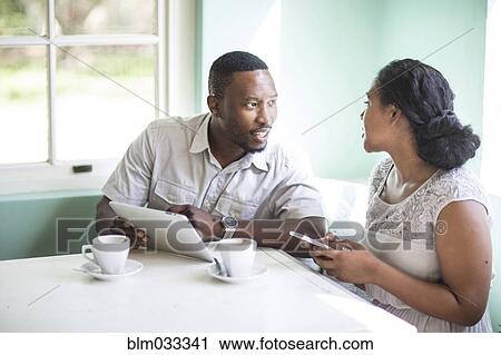 Stock Image - Couple using cell phone and digital tablet at breakfast table. Fotosearch