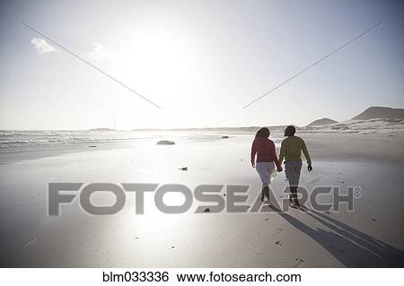 Stock Photograph - Couple walking on beach. Fotosearch