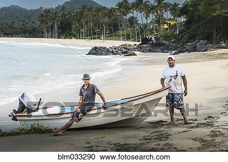 Stock Image - Friends standing near boat on beach. Fotosearch