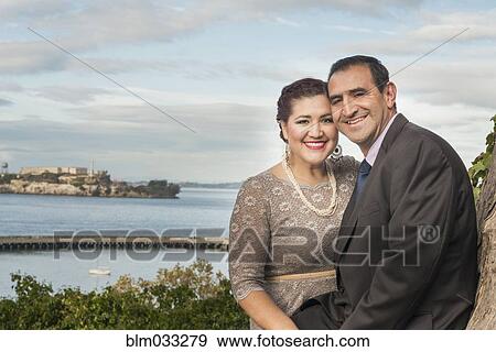 Stock Photo - Hispanic couple in formal wear smiling near waterfront. Fotosearch